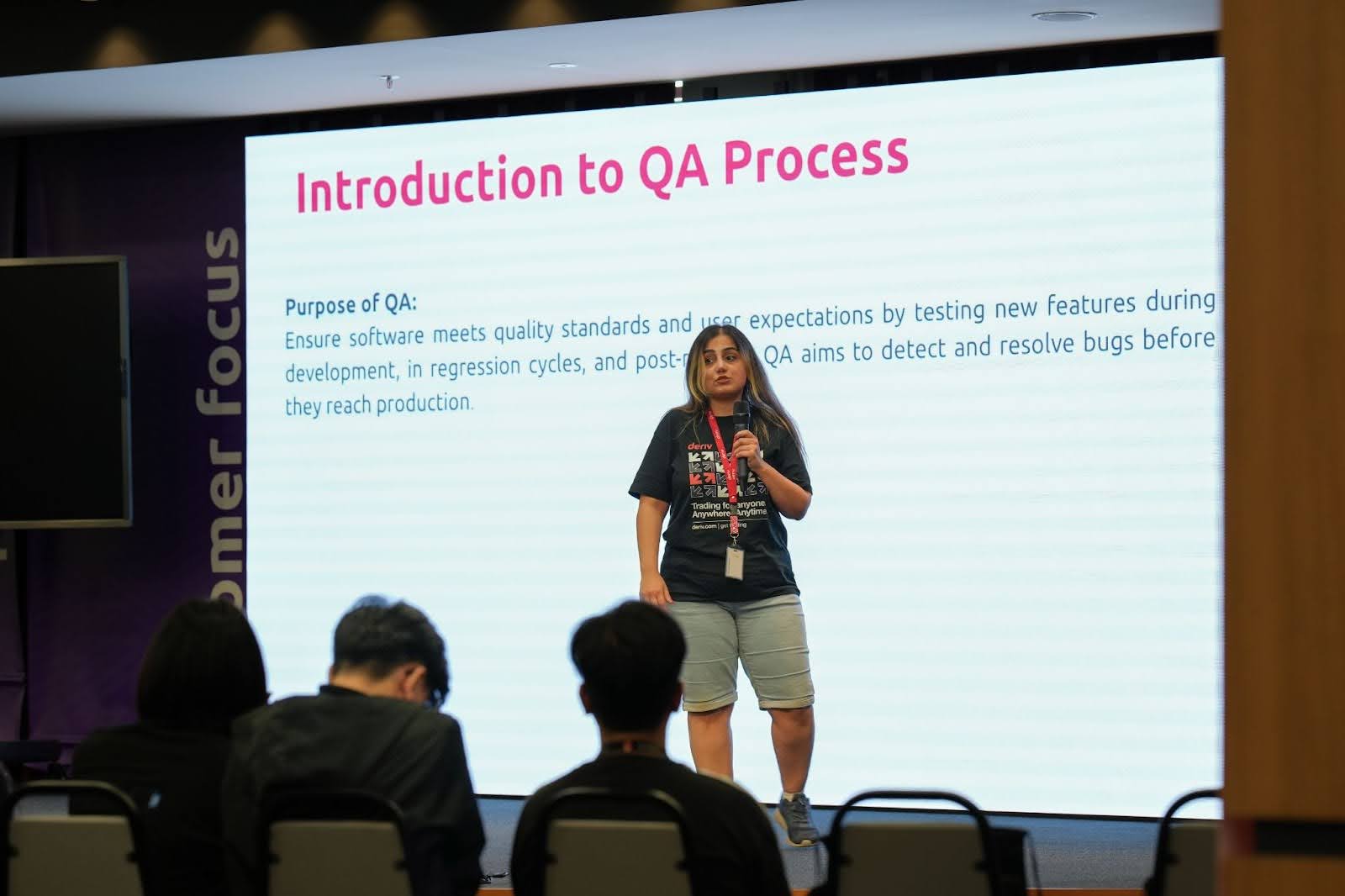 A Deriv QA team member stands in front of a screen, presenting the QA process to an audience.
